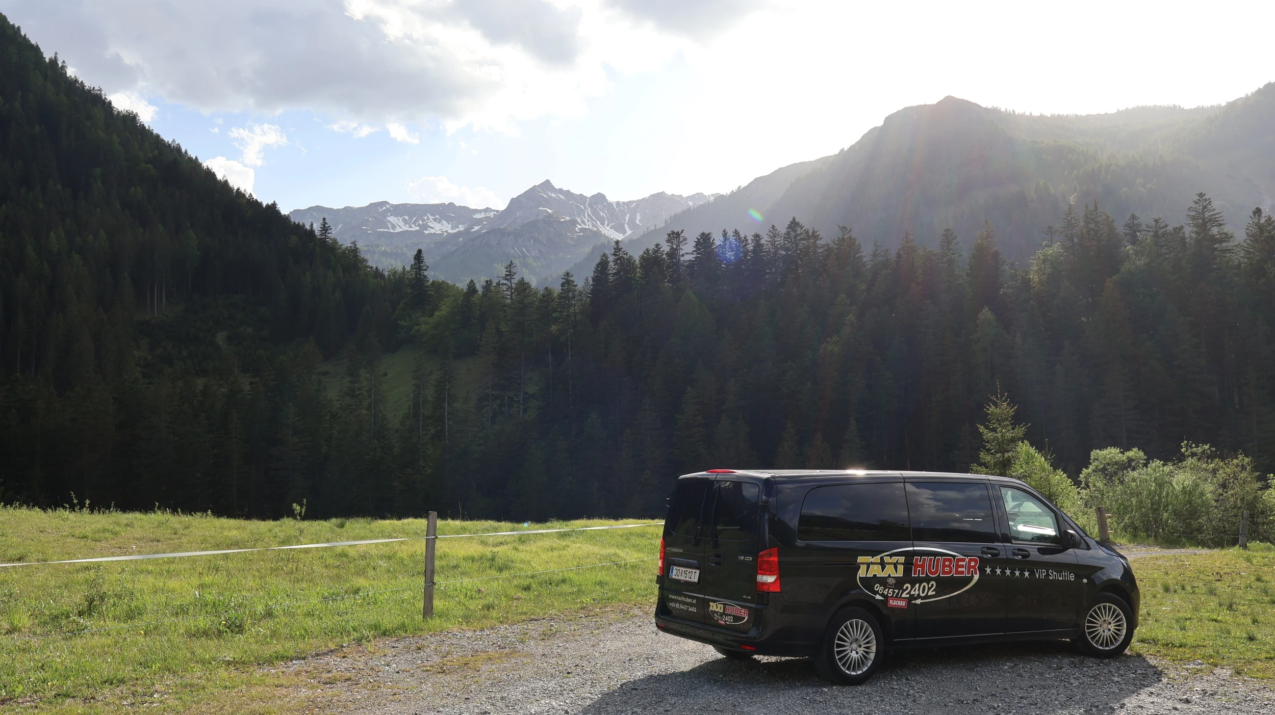 Ein Taxi der Firma Taxi Huber steht vor einer grünen Wiese und einer Bergsilhouette in Flachau.