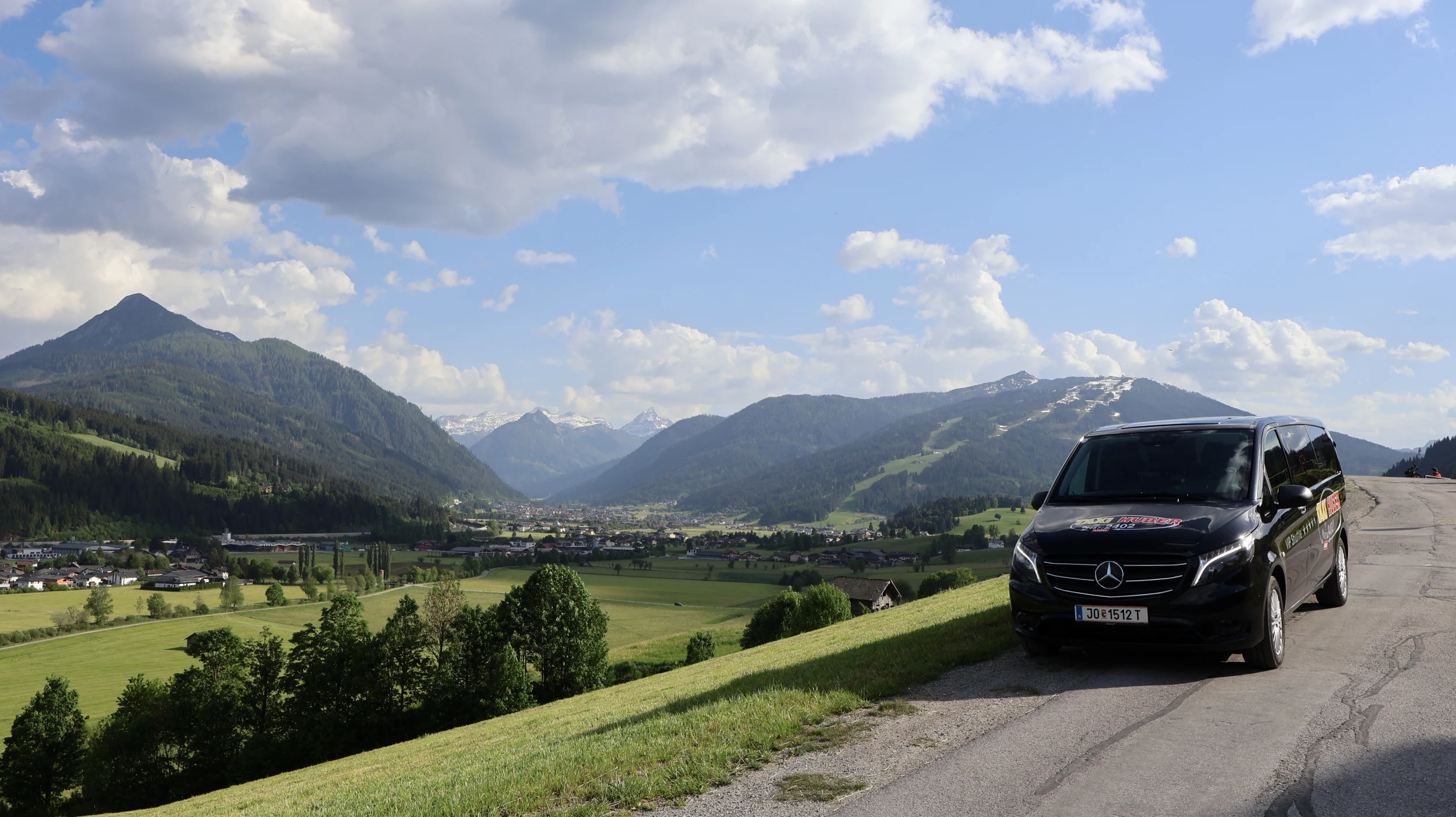 Ein Taxi der Firma Taxi Huber auf einer Bergstraße mit Blick auf Flachau.